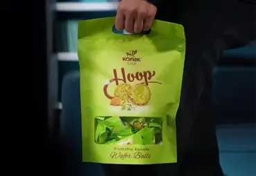 Person holding a green Konak Hoop Pistachio Kunafa Wafer Balls pouch with visible wrapped pieces inside.